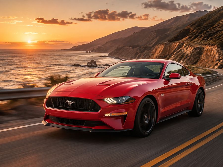 Red muscle car coupe on a coastal road at sunset