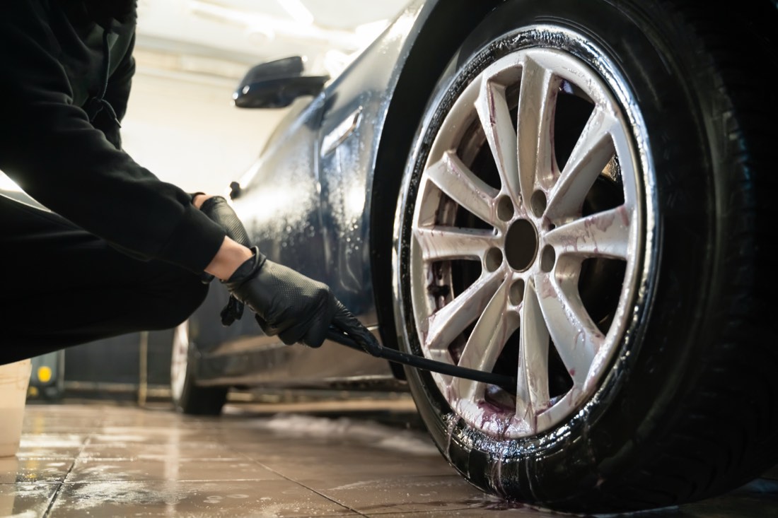 Detailer cleaning a car wheel with a brush